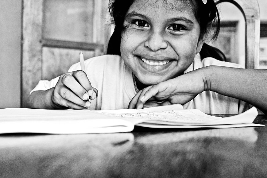 Smiling Young Student Girl Writing In Notebook At School Desk