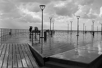 Black and white rainy pier with people and umbrellas