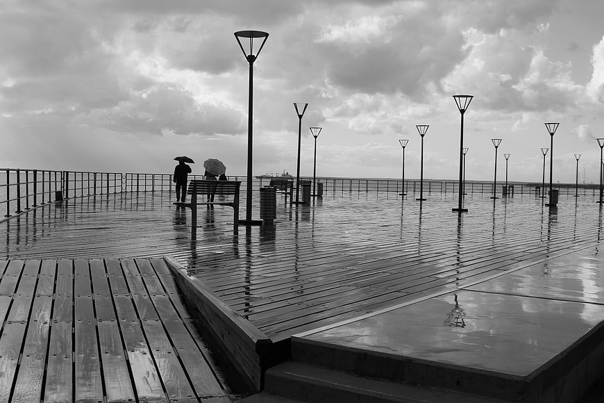 Black and white rainy pier with people and umbrellas