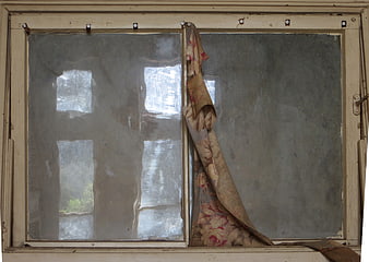 Old weathered window with tattered floral curtain