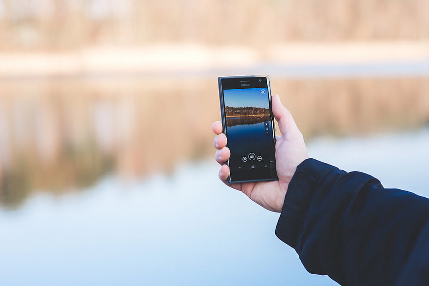 Hand holding smartphone taking photo of lake landscape