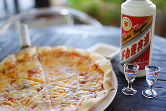Cheese pizza and Moutai liquor bottle with two glasses on a wooden table