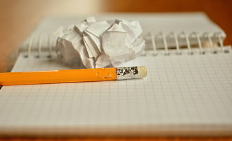 Yellow pencil and crumpled paper ball on grid notebook