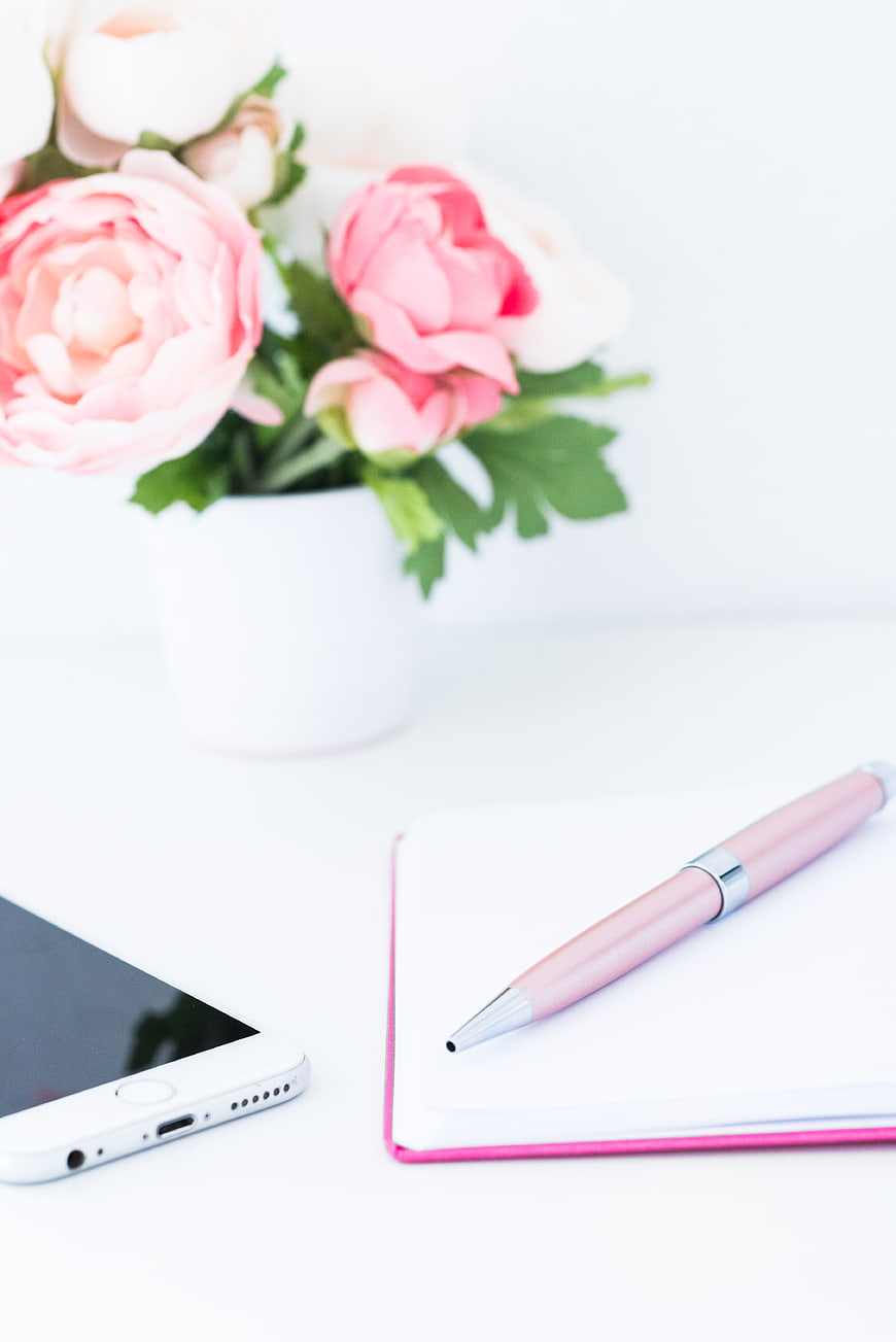 Pink Pen, Notebook, and Smartphone on White Desk with Flowers