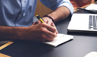 Close-up of hands writing on notepad at office desk
