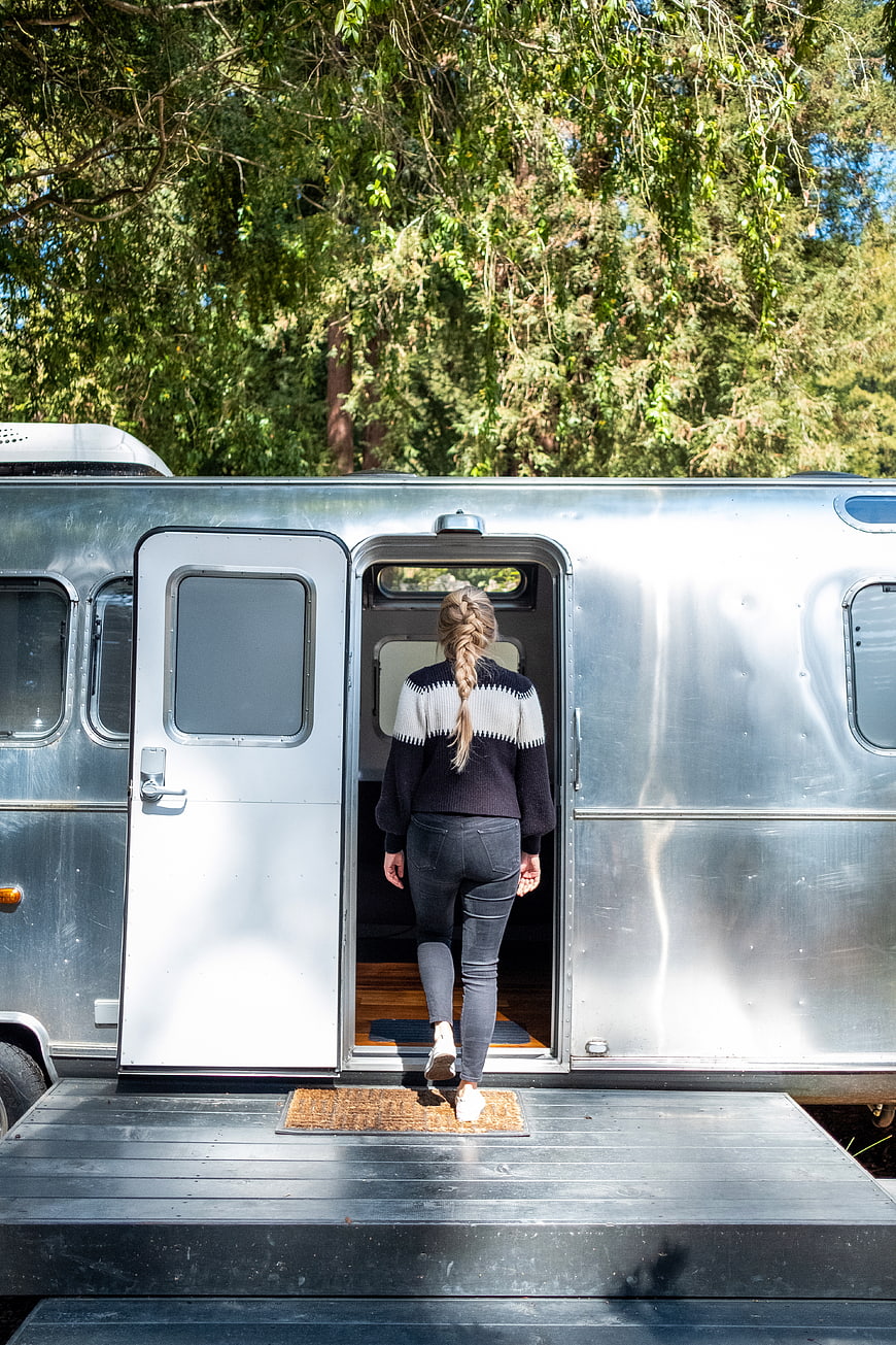 Woman entering vintage silver Airstream camper in forest