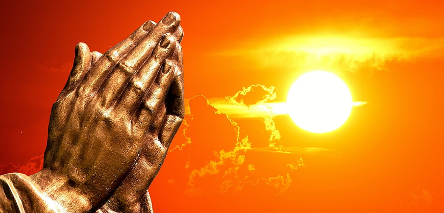 Golden Praying Hands Statue Against Vibrant Orange Sunset Sky