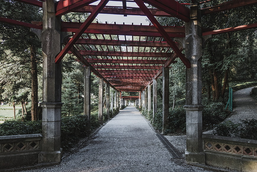 Red metal pergola walkway in a lush green garden