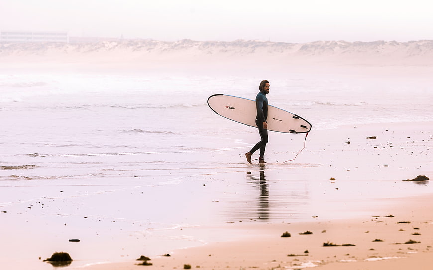 Surfer walking on misty beach with surfboard