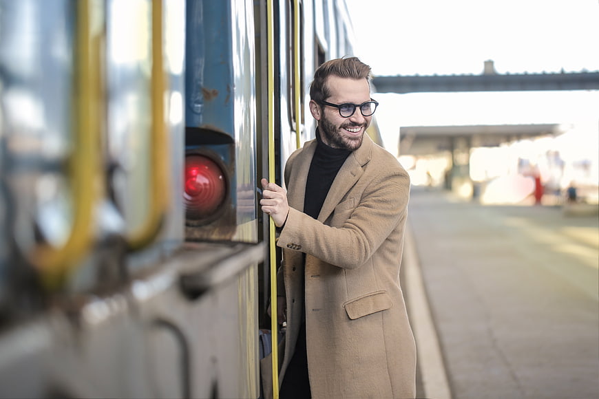 Smiling man in beige coat boarding train at station