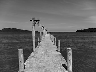 Black and white photo of a long concrete pier extending into the sea