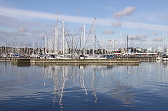 Sailboat masts reflecting in calm harbor water under blue sky