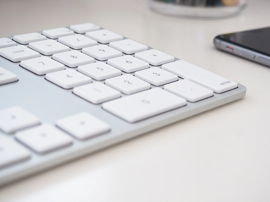 Close-up of white computer keyboard and smartphone on desk