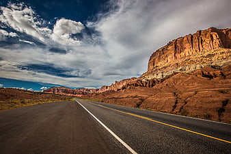 Scenic desert highway winding through red rock canyons under dramatic sky