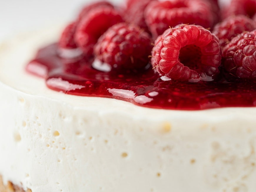 Close-up of creamy cheesecake topped with fresh raspberries and red sauce