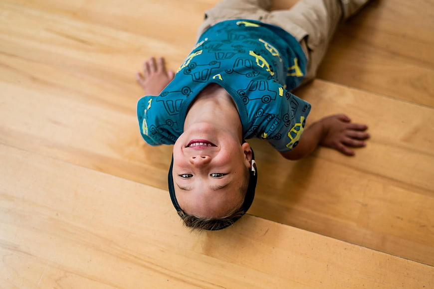 Happy Boy Lying Upside Down on Wooden Floor
