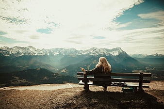 Woman Sitting on Bench Overlooking Snowy Mountain Range