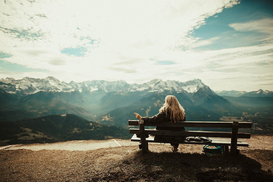 Woman Sitting on Bench Overlooking Snowy Mountain Range