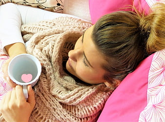 Woman resting in bed with scarf and heart mug