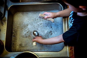 Child washing dishes in soapy kitchen sink