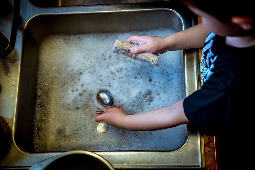 Child washing dishes in soapy kitchen sink
