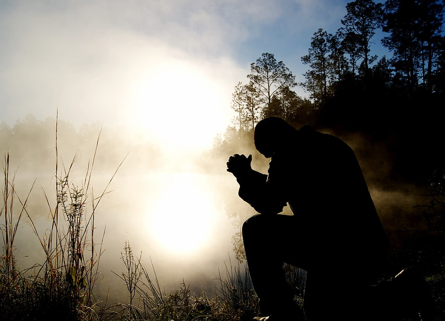 Silhouette of Man Praying in Misty Forest at Dawn