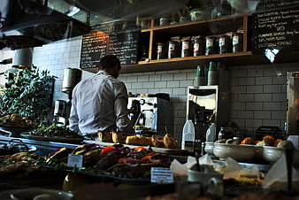 Barista preparing coffee in busy cafe kitchen with food display