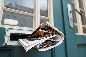 Stack of newspapers overflowing from a teal residential letterbox