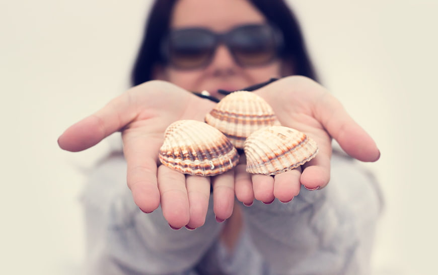 Woman holding seashells in cupped hands on beach