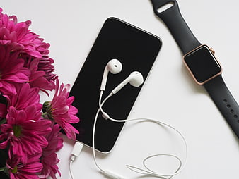 Flat lay of smartphone, headphones, smartwatch, and pink flowers
