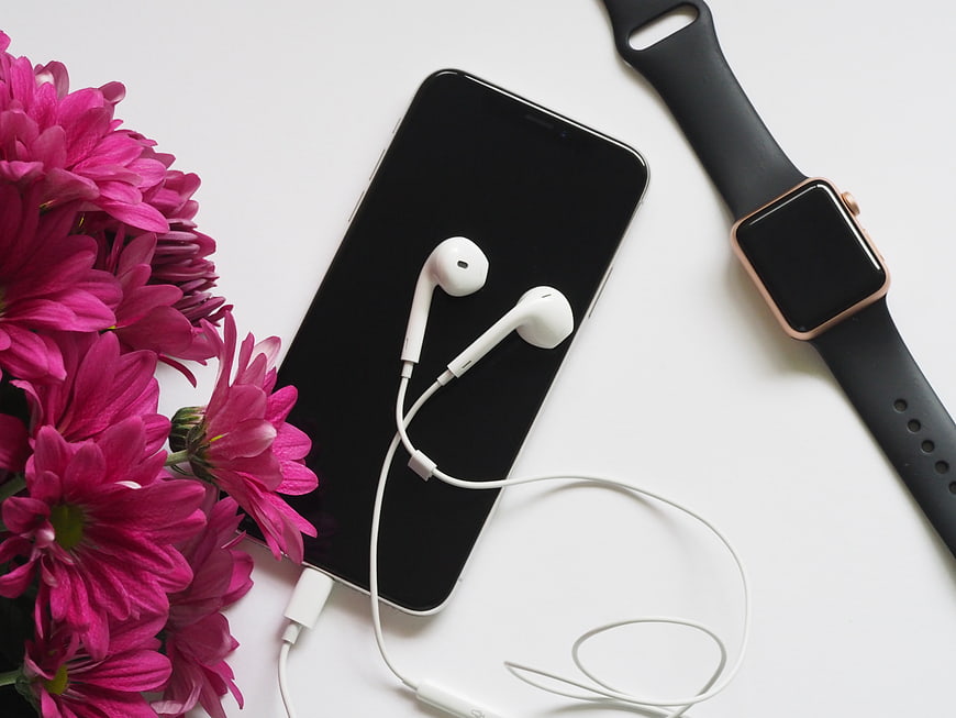 Flat lay of smartphone, headphones, smartwatch, and pink flowers