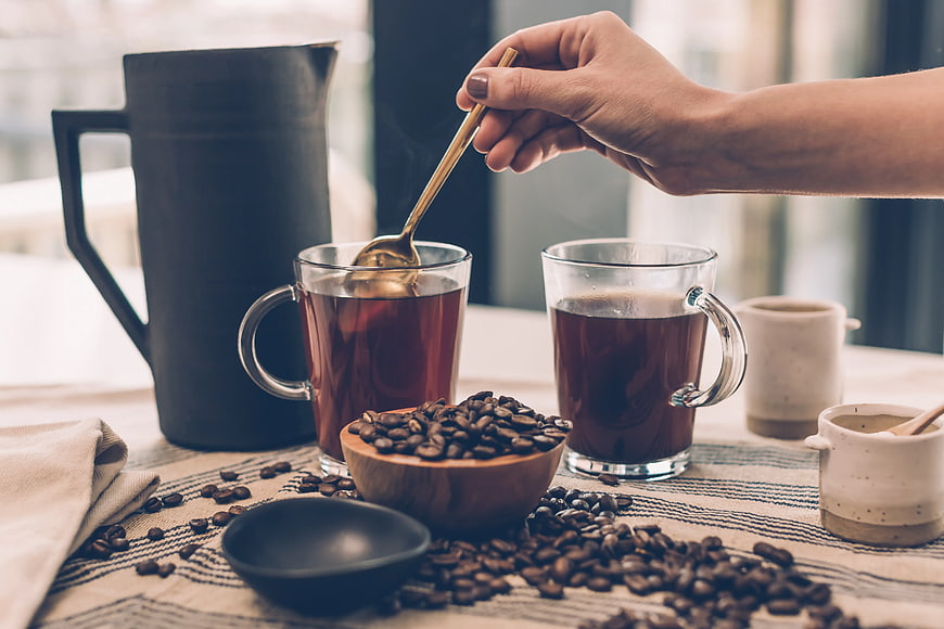 Hand Stirring Coffee in Glass Mug with Beans