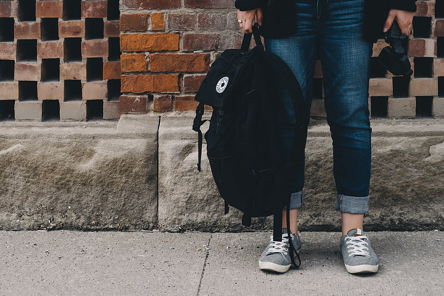 Person with Backpack and Camera Against Brick Wall