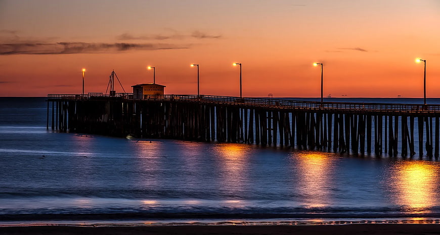 Silhouetted Wooden Pier at Sunset with Glowing Streetlights