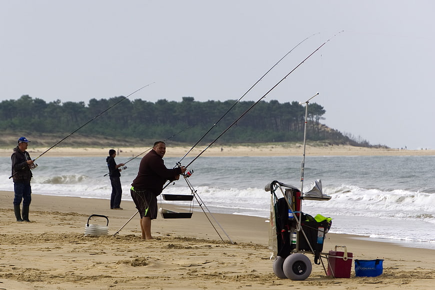 Surf fishermen casting rods on sandy beach with ocean waves