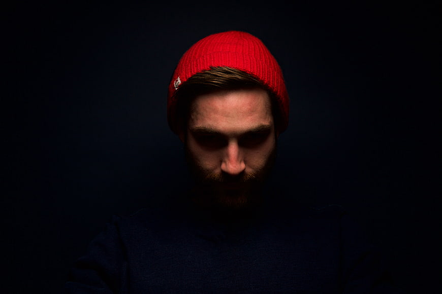 Portrait of man in red beanie looking down in dark lighting