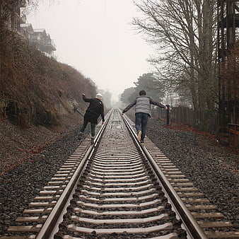 Two friends walking away on foggy railroad tracks