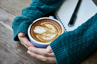 Hands holding latte with heart art in teal sweater