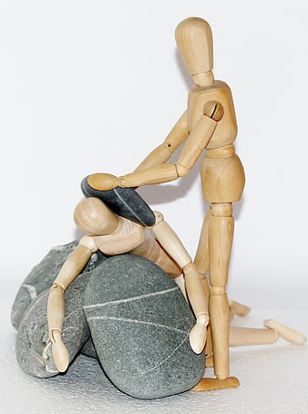 Wooden mannequin helping fallen figure with stones