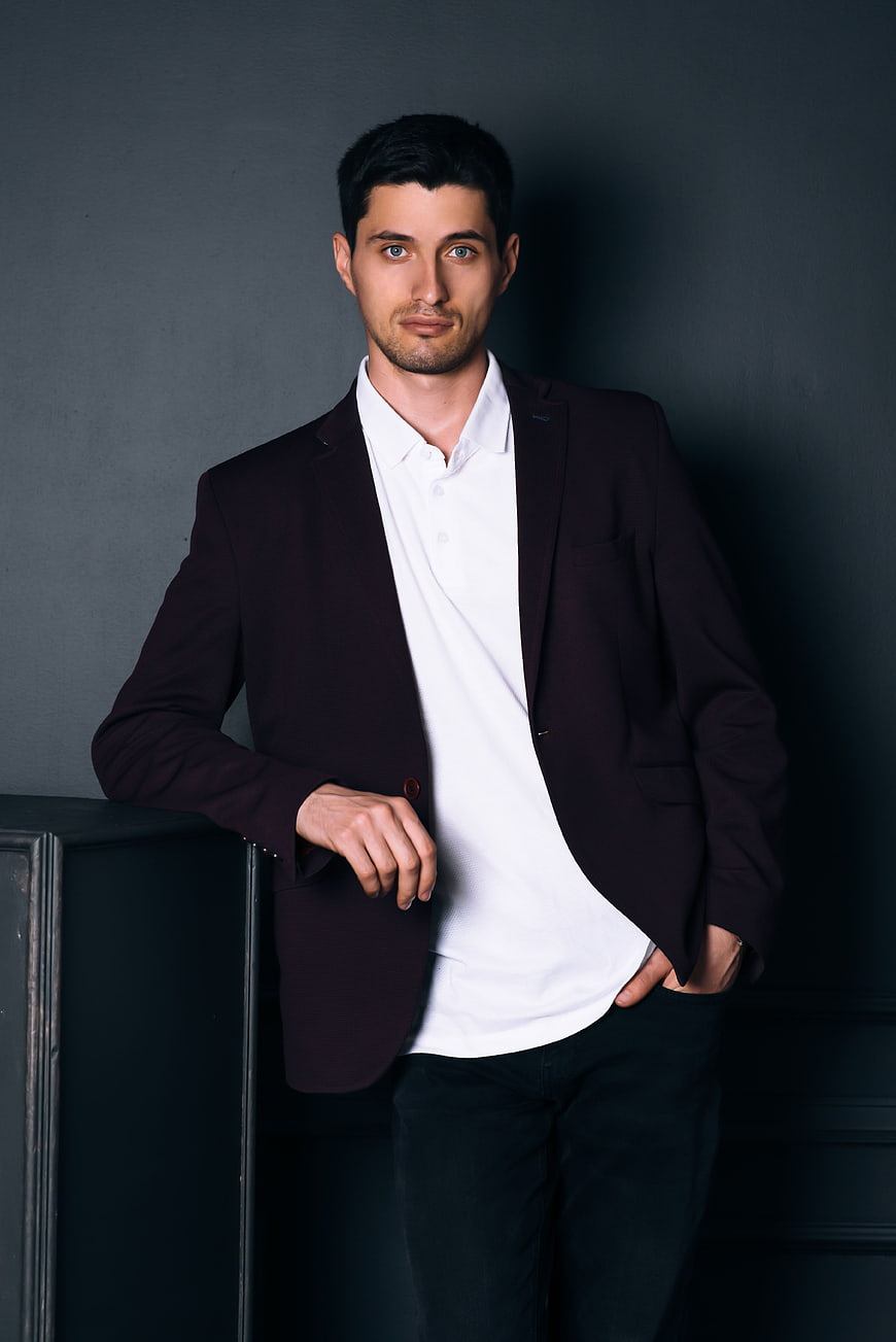 Confident man in burgundy blazer leaning against dark wall