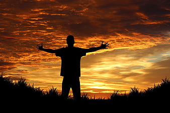 Silhouette of Man with Arms Raised Against Dramatic Sunset Sky