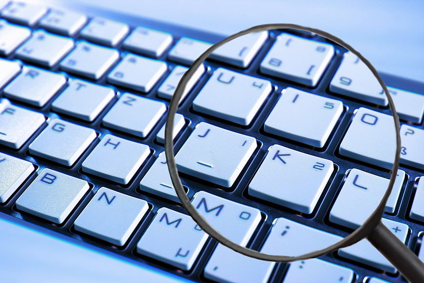 Magnifying glass inspecting computer keyboard keys for security
