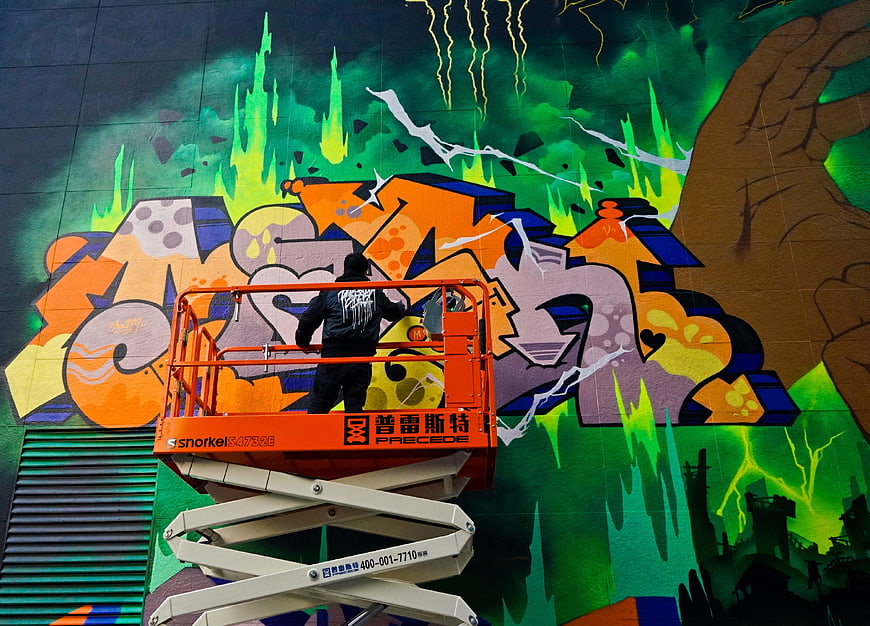 Graffiti artist painting colorful mural on lift
