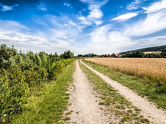Gravel path through rural landscape with wheat field and blue sky