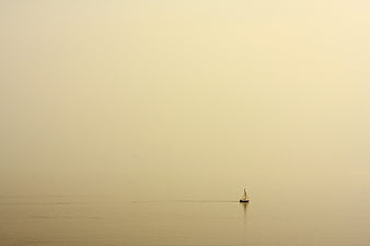 Lone sailboat on calm water in hazy golden light