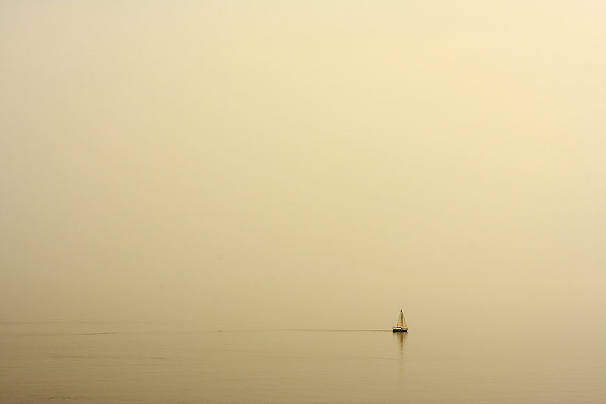 Lone sailboat on calm water in hazy golden light