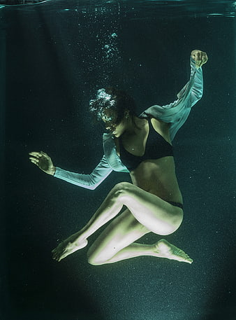 Underwater fashion portrait of a woman in a black bikini and flowing white top