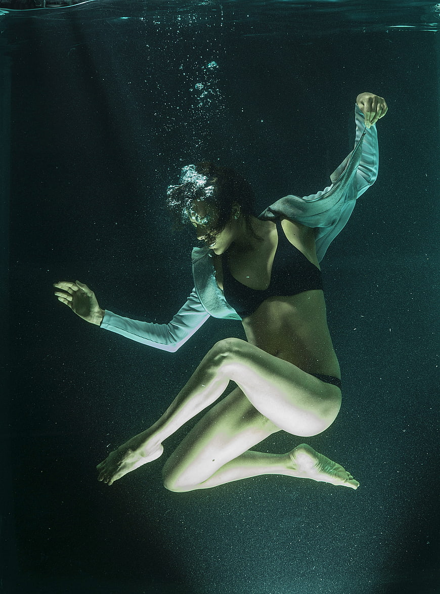 Underwater fashion portrait of a woman in a black bikini and flowing white top