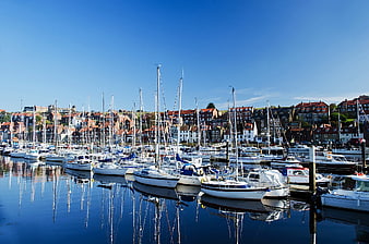Sailboats docked in a harbor with coastal town reflections