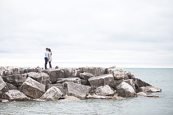 Couple standing on rocky jetty by the ocean